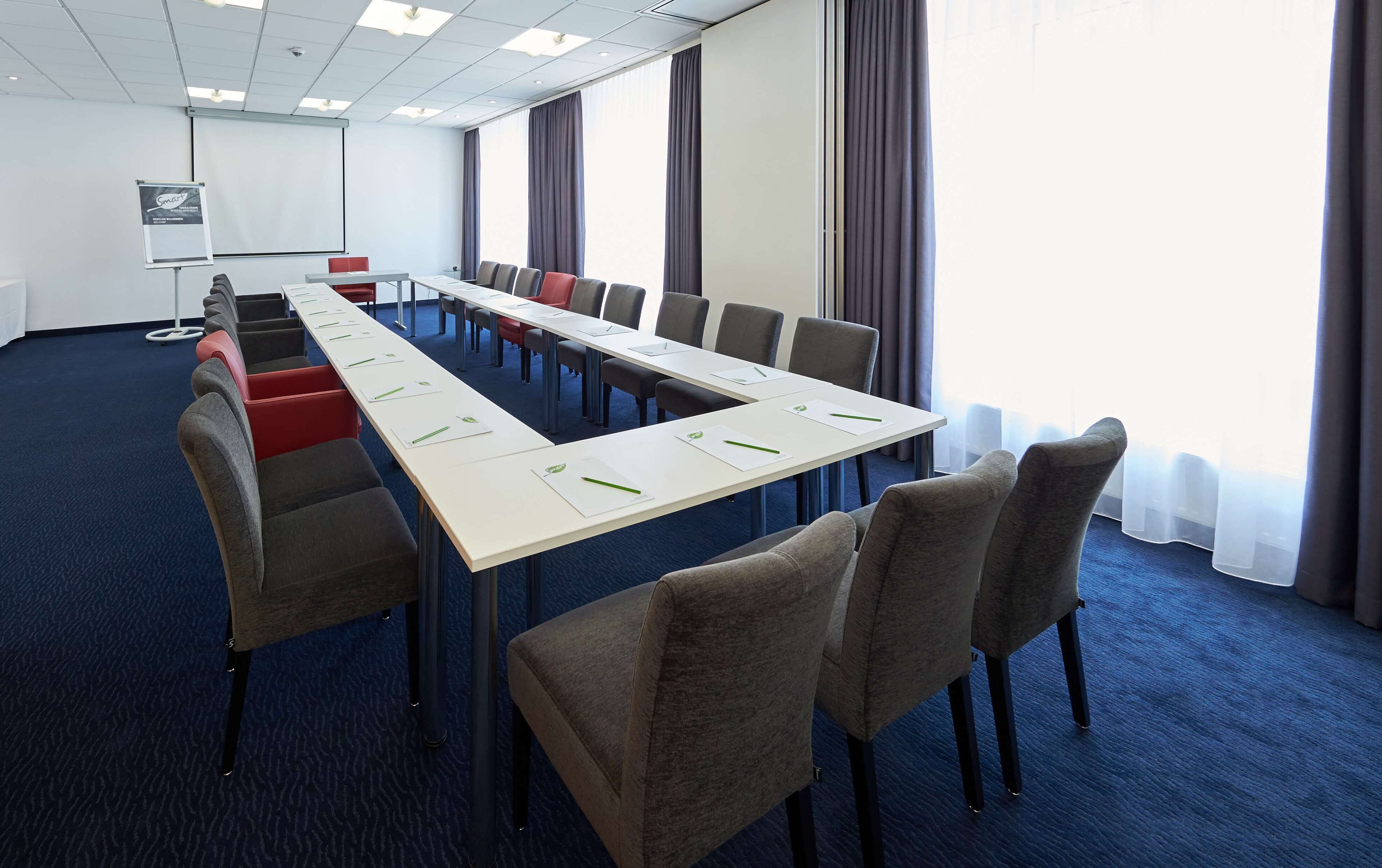A conference room with a long table, chairs, a projector screen, and a whiteboard.