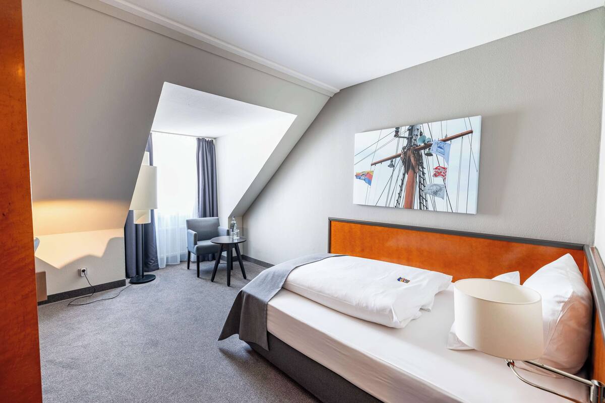 A hotel room with a bed, a desk, a chair, and a painting on the wall.