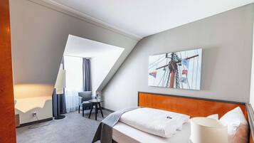 Ett hotellrum med en säng, ett skrivbord, en stol och en tavla på väggen.