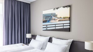 A hotel room with two beds, a large window with curtains, a painting of a yacht, and a nightstand with a lamp. - Atlantic Hotel Vegesack (Bremen)