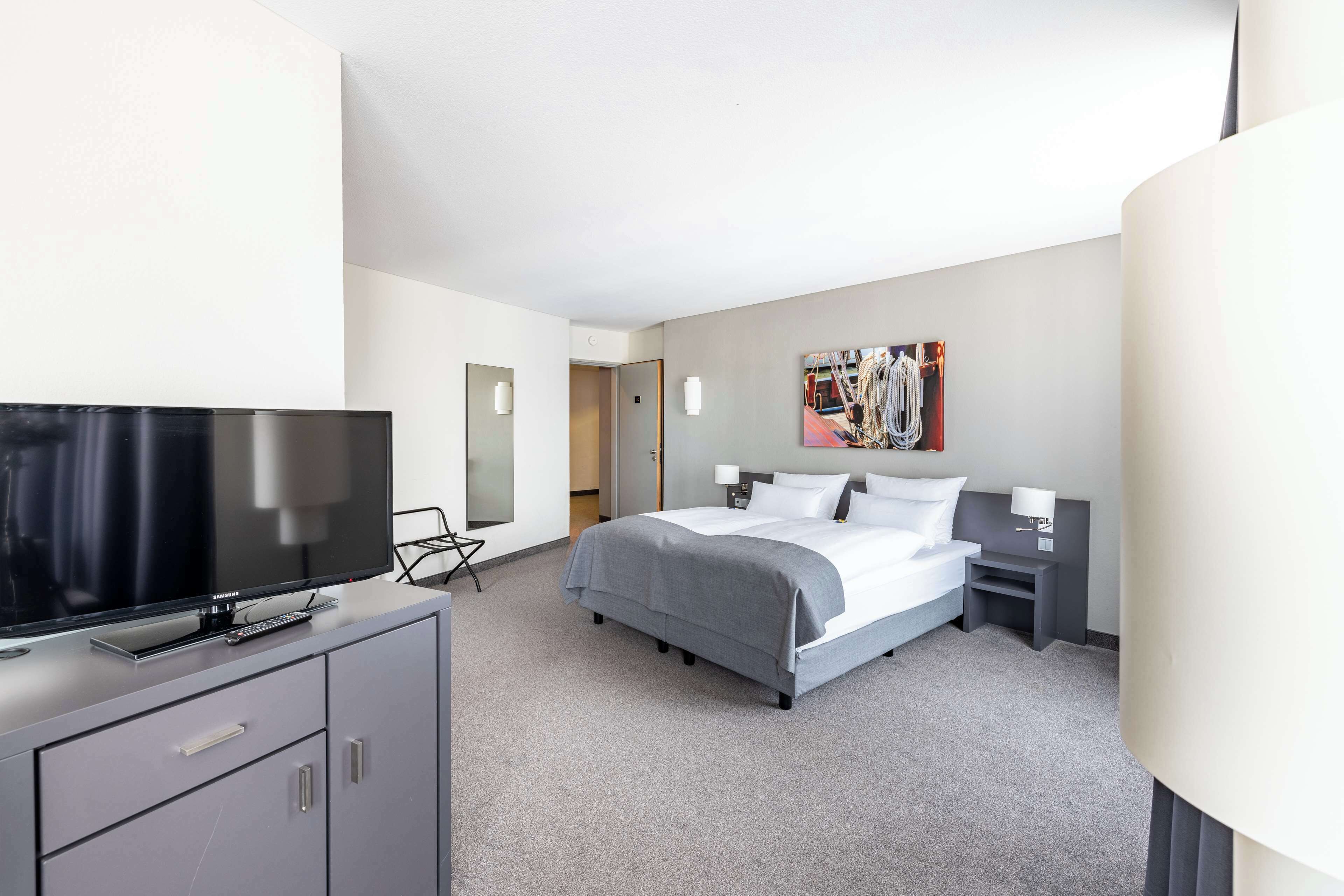A modern hotel room with a large bed, a flat-screen TV, a desk, and a chair.