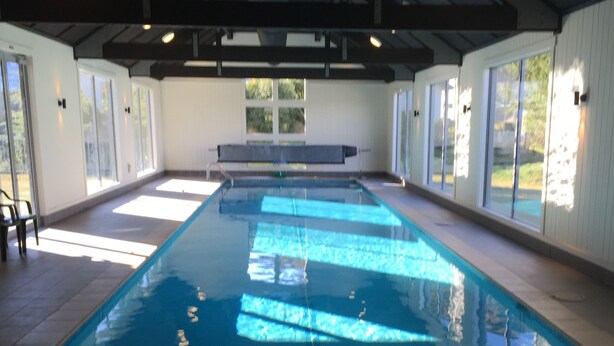 An indoor swimming pool with clear blue water, large windows, and a bench along the side. - Arrowfield Apartments (Arrowtown)