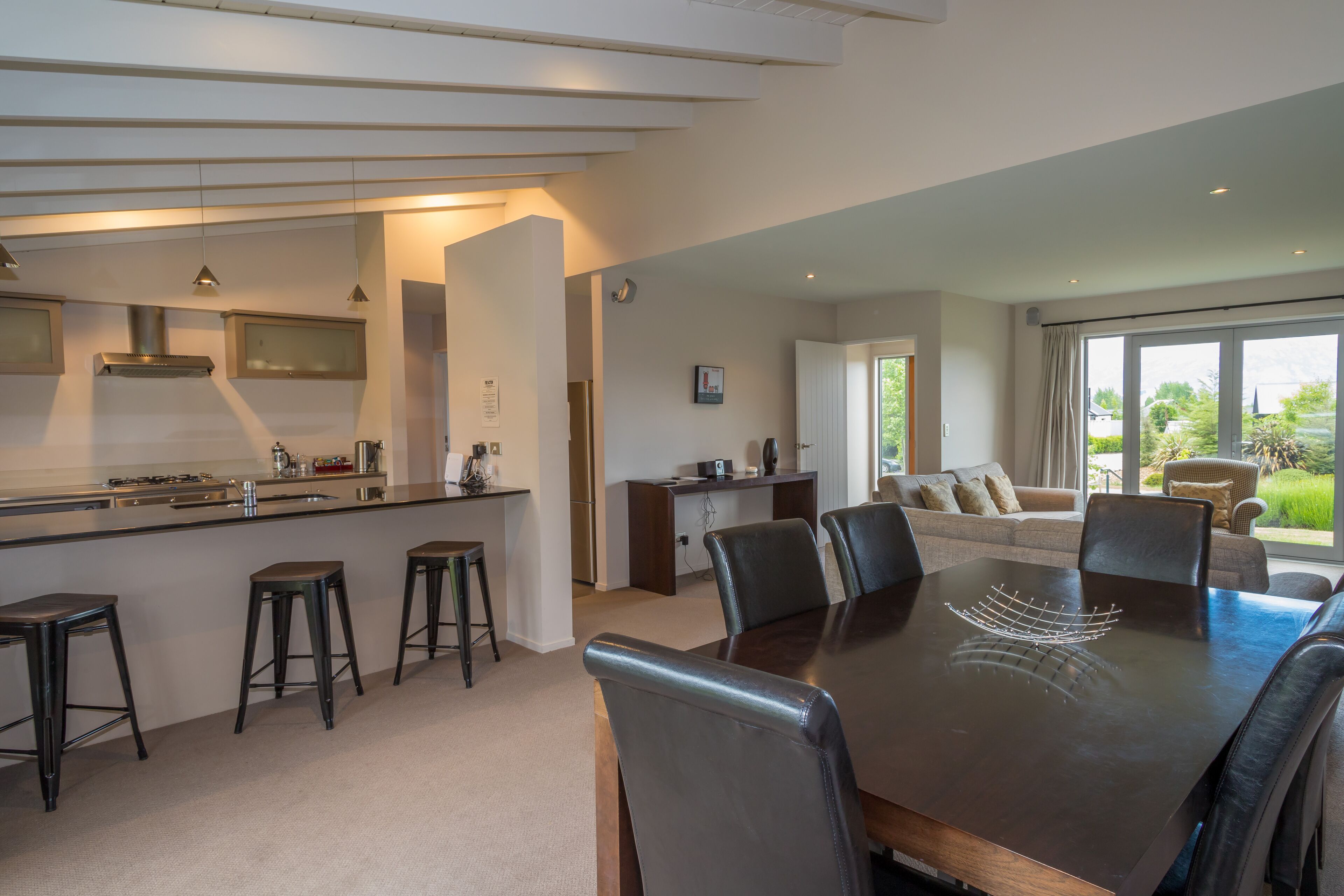 Een moderne keuken met een centraal eiland, een eetgedeelte met een grote tafel en stoelen, en een woonkamer met een bank en uitzicht op de omgeving.