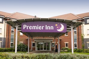 L’entrée d’un hôtel, avec une enseigne lumineuse indiquant « Premier Inn » et un symbole représentant un croissant de lune.