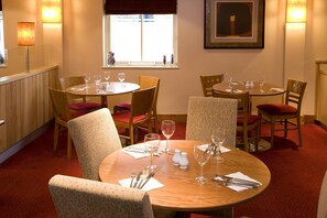 A dining area with round tables, chairs, and empty wine glasses. - Premier Inn Heathrow Airport - M4/J4 (Hayes)