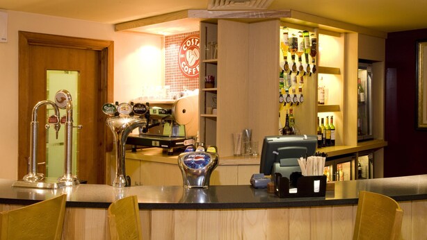 A bar area with a counter, stools, and a variety of bottles. - Premier Inn Heathrow Airport - M4/J4 (Hayes)