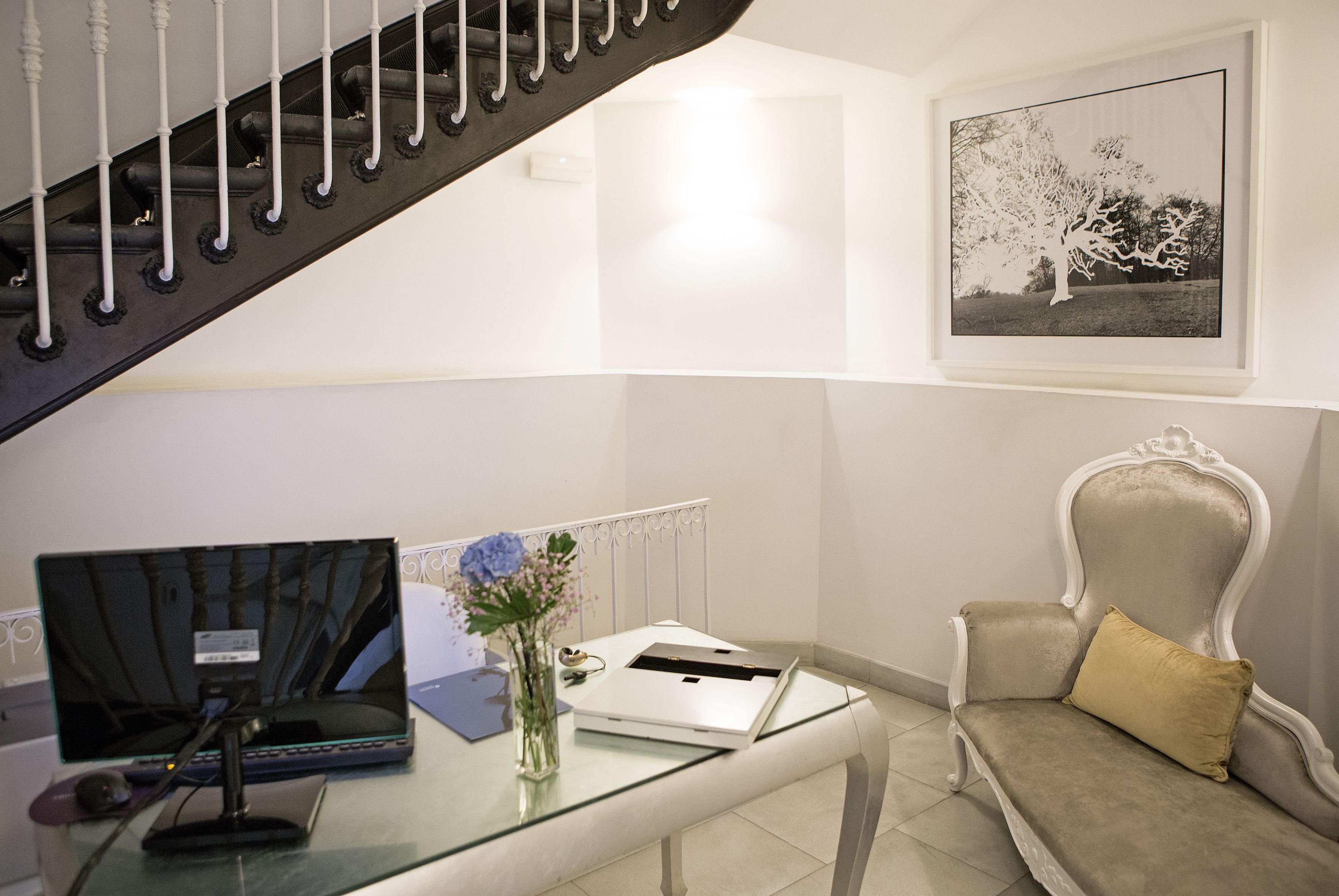Un salon moderne avec une table basse en verre, un ordinateur portable, un vase de fleurs, un canapé avec un coussin et un tableau encadré accroché au mur.