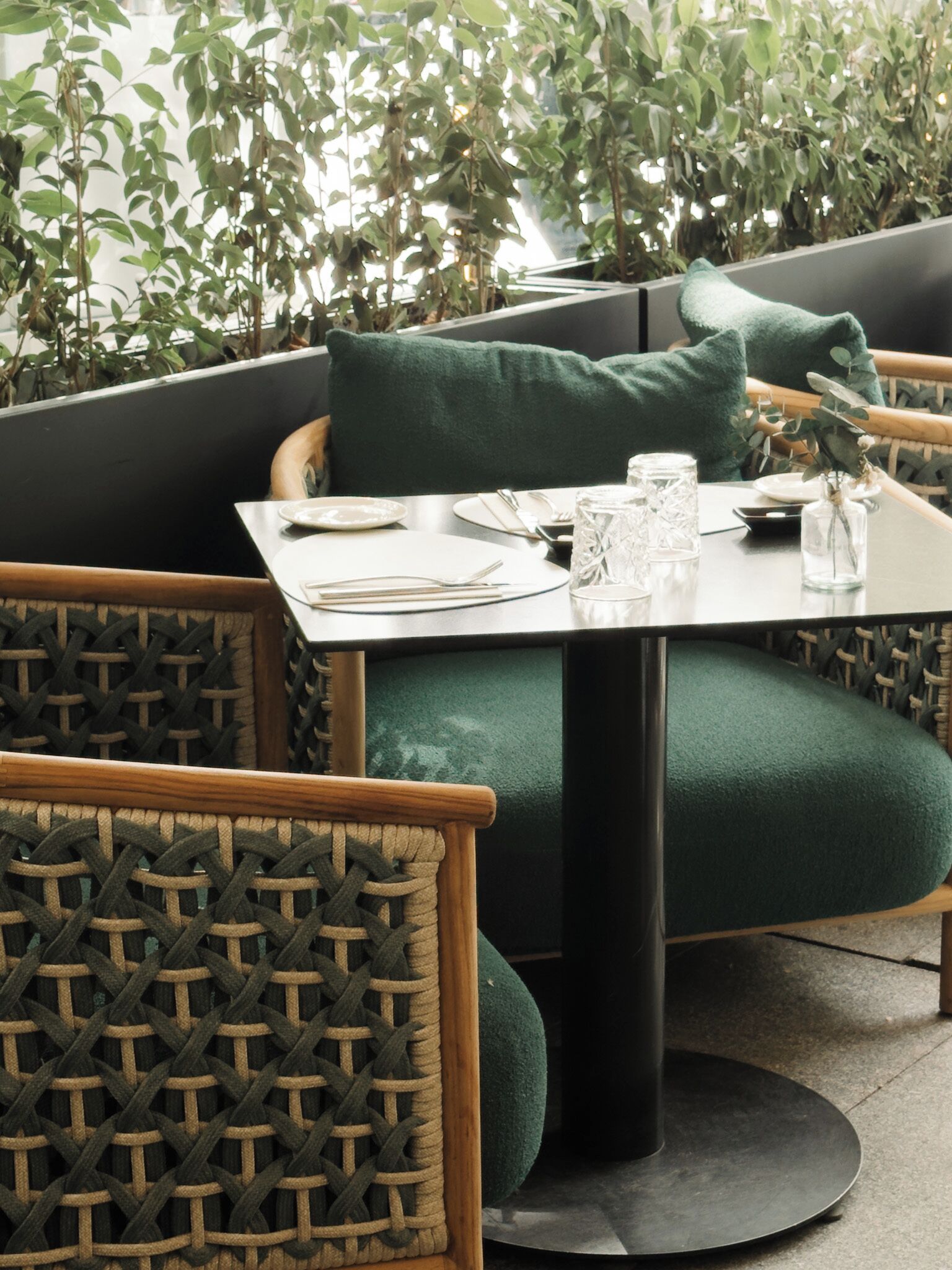 Comedor con una mesa dispuesta para dos, rodeado de sillas de mimbre y asientos tapizados en verde.