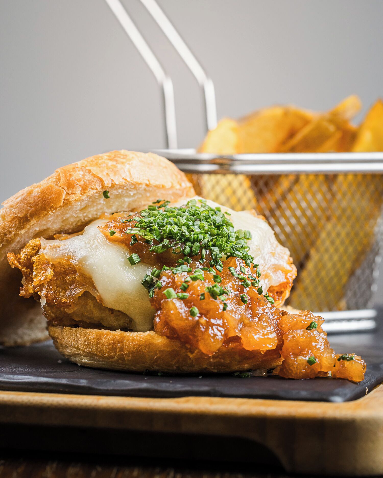 Un sandwich avec un pain croustillant, du fromage fondu et une garniture d’oignons caramélisés et d’oignons verts.