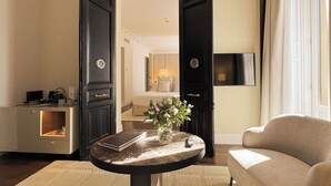 Habitación de hotel con cama, televisor, una mesita de café con un libro y flores, y un sofá.