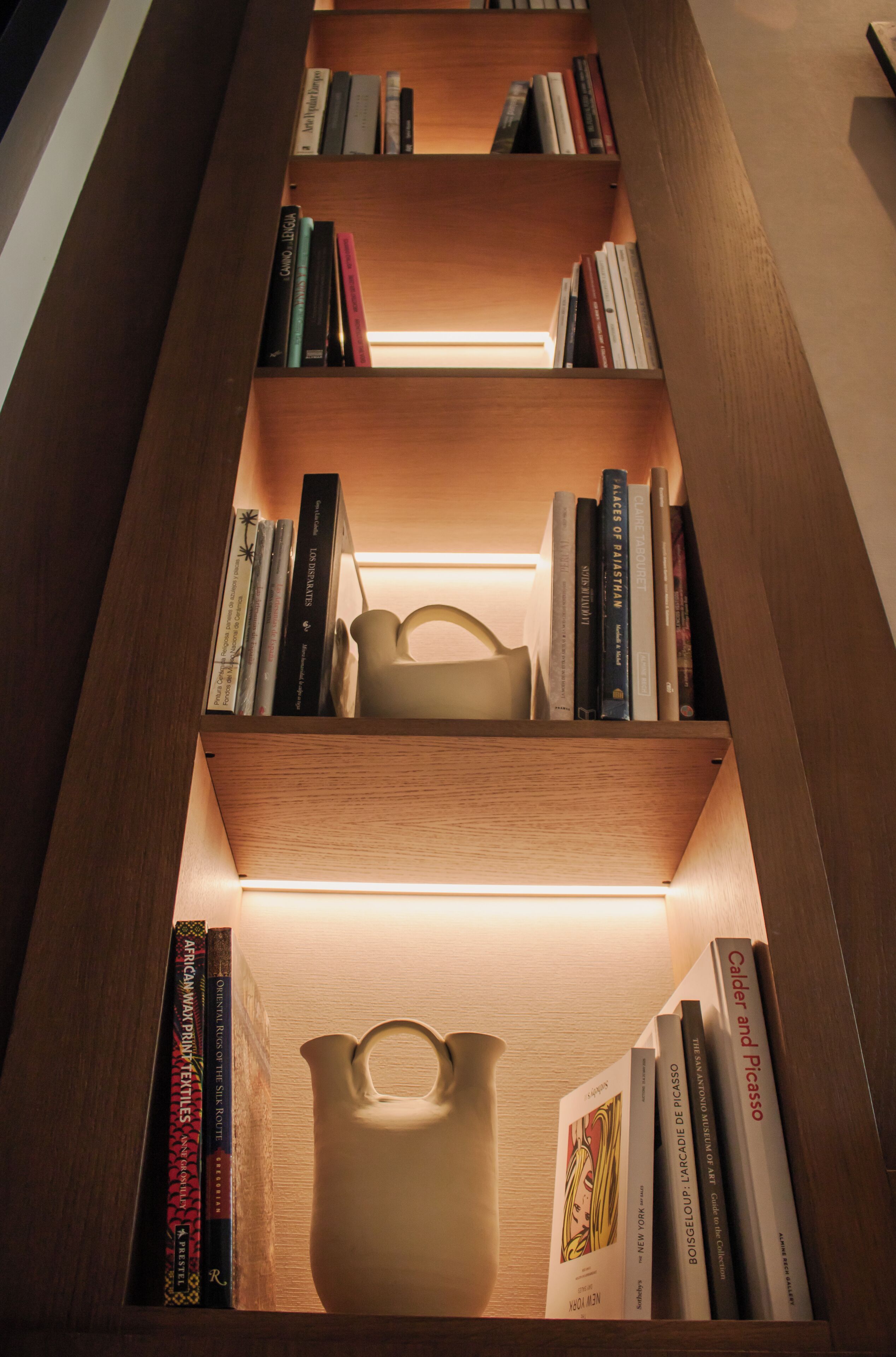 A bookshelf with multiple compartments, each containing books and a ceramic pitcher.