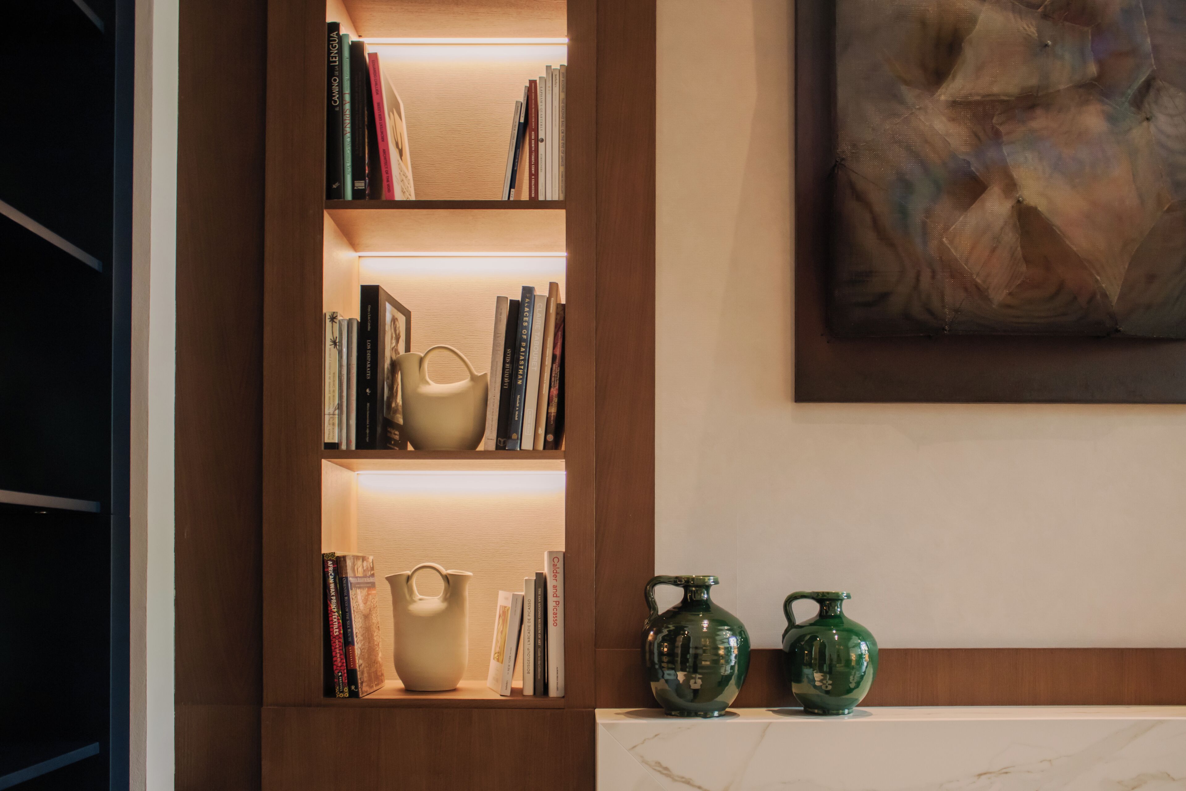 A bookshelf with books and decorative items, a marble fireplace, and a painting on the wall.