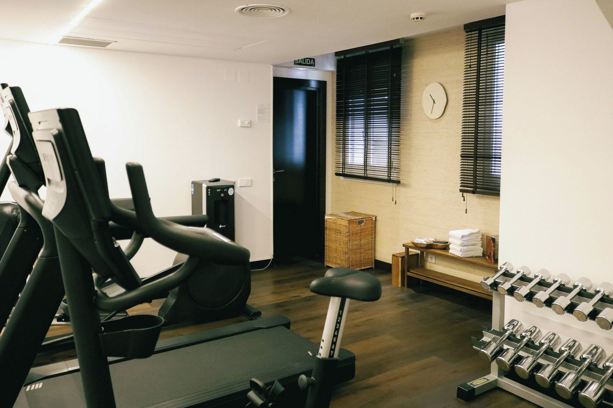 Une salle de sport équipée de matériel d’exercice, une horloge au mur et une porte portant l’inscription « SORTIE ».