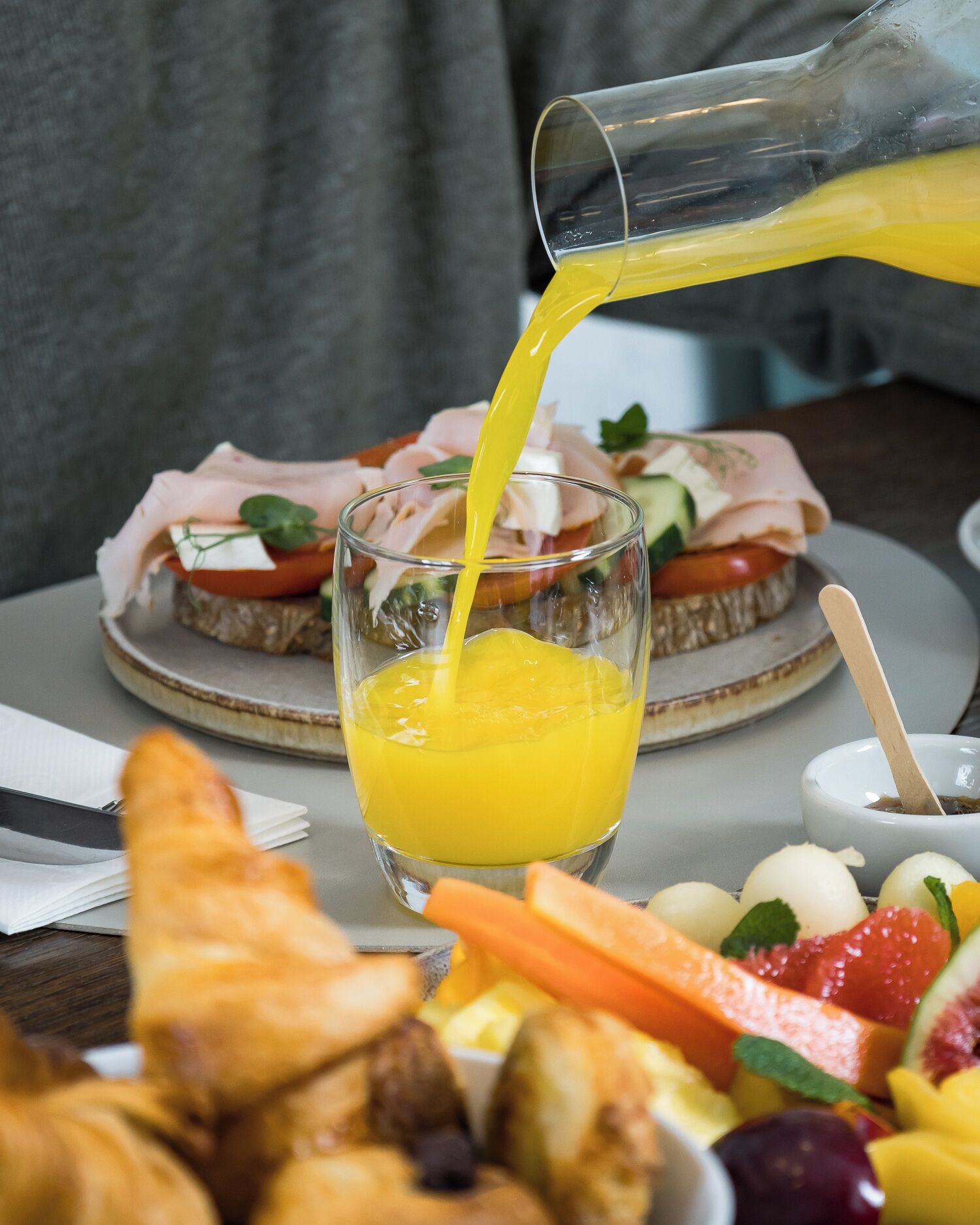 Een ontbijtsetting met een glas sinaasappelsap, een belegd broodje, croissants en een fruitschaal.