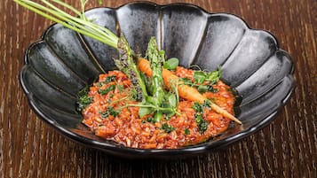 A black, scalloped-edge dish with a red sauce and vegetables on a wooden table.