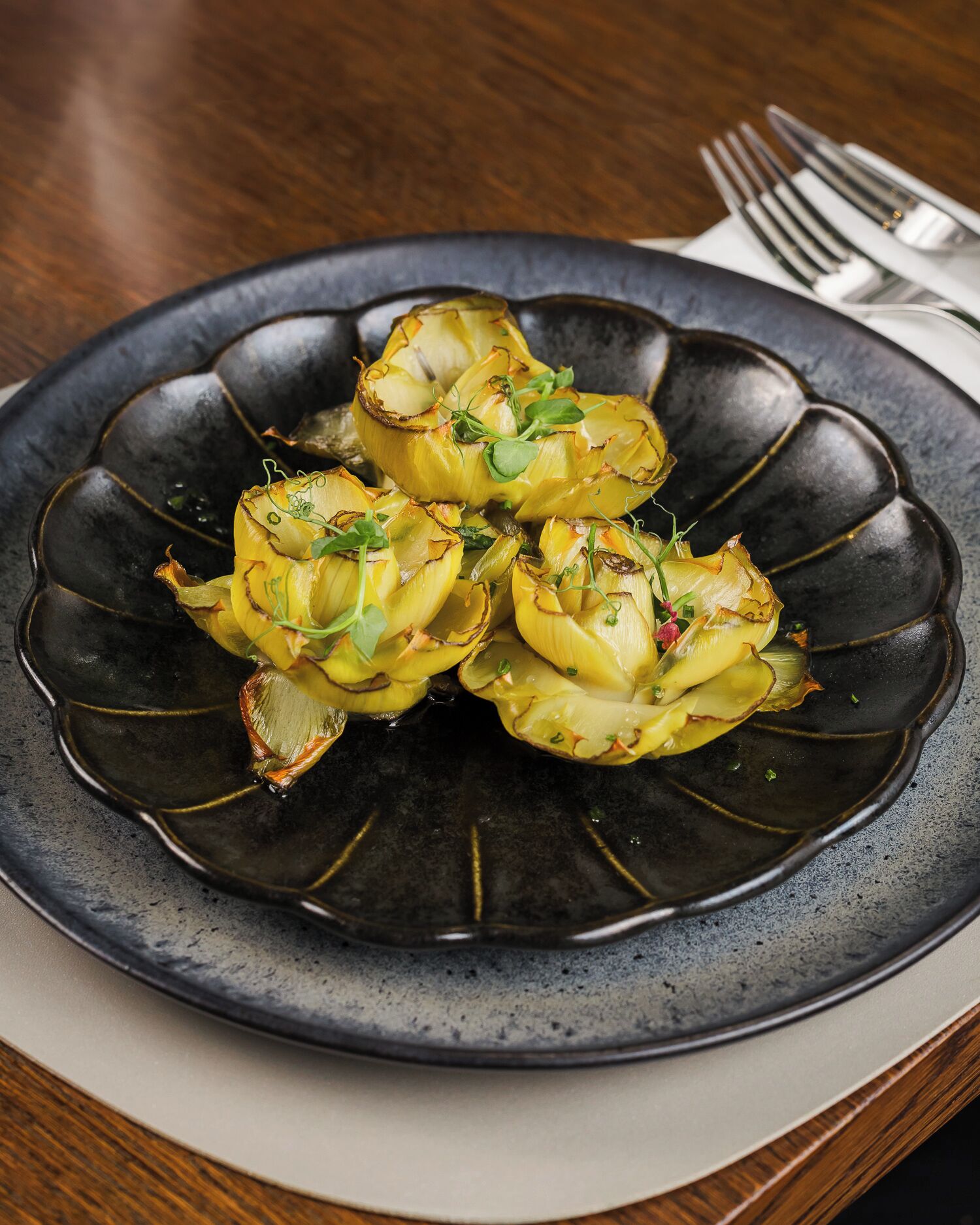 A plate of artichoke hearts garnished with herbs, served on a dark ceramic plate.