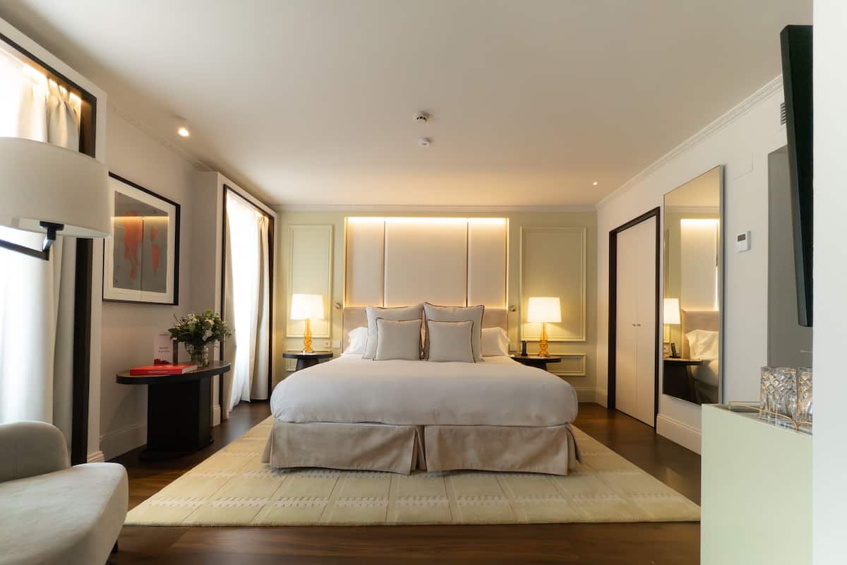Hotelkamer met een groot bed, nachtkastjes, een stoel, een spiegel en uitzicht op de gang.
