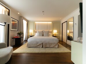 Ein Hotelzimmer mit einem großen Bett, Nachttischen, einem Sessel, einem Spiegel und Blick auf den Flur.