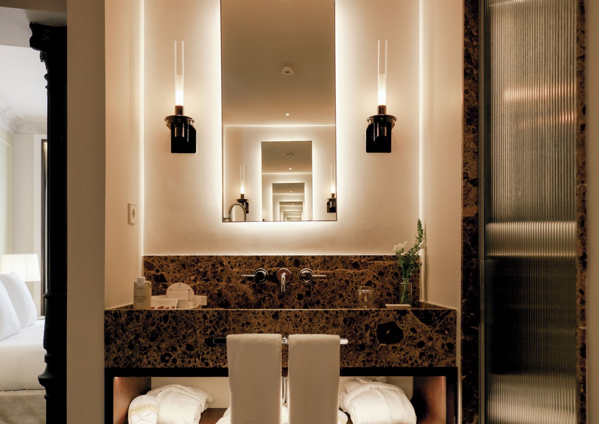 A bathroom with a granite countertop, two sinks, a large mirror, and two wall-mounted lights.
