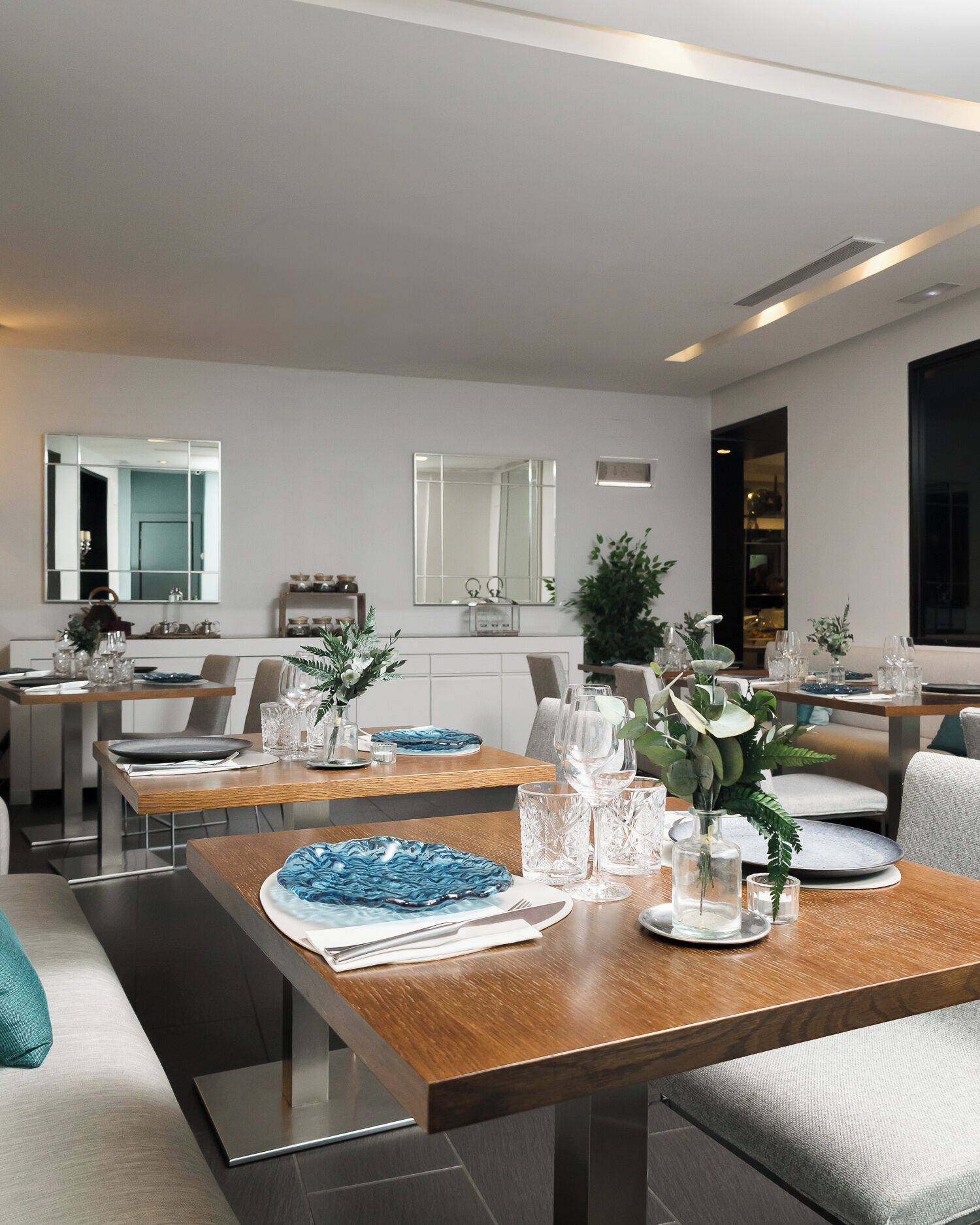 A modern dining area with wooden tables, glassware, and decorative plants.