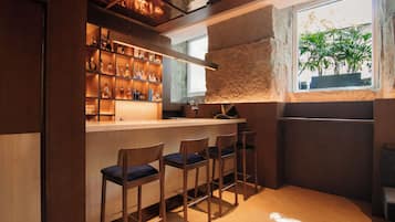 Eine Bar mit Holzhockern, einem Flaschenregal und einem Fenster mit Blick auf Grünflächen.