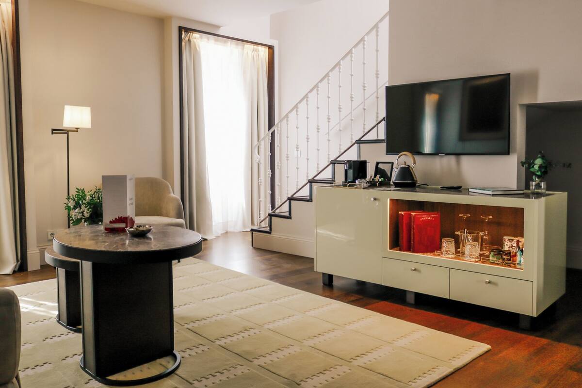 Een moderne woonkamer met een flatscreen televisie, een ronde salontafel, een bank, een trap en een kast met decoratieve objecten.