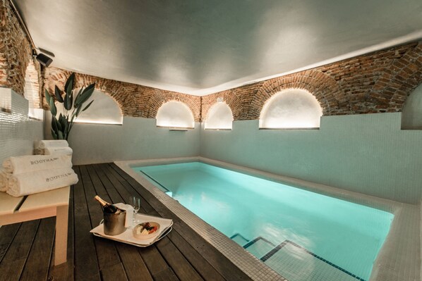 Un área de spa con piscina, terraza de madera y pared de ladrillo con ventanas de arco.