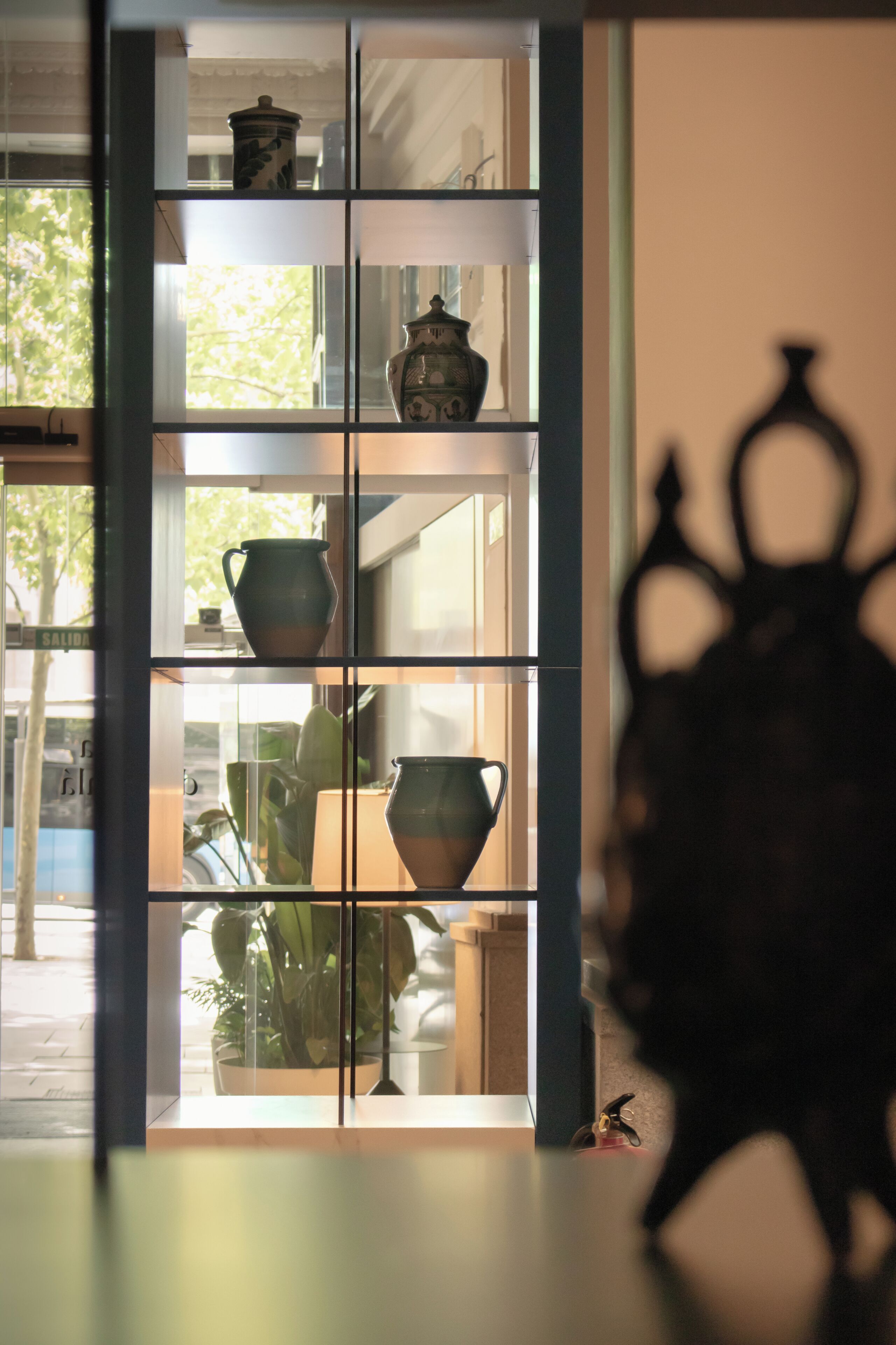 A room with a window, shelves with decorative items, and a silhouette of a person.
