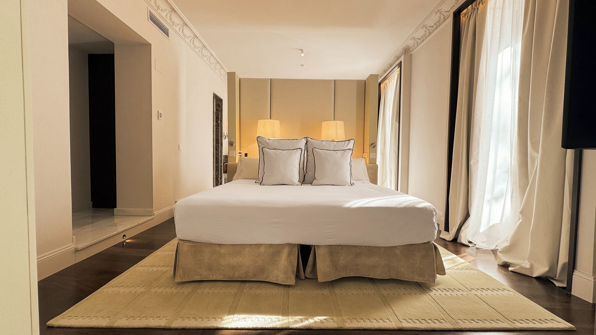 Ett hotellrum med en stor säng, två sänglampor, en spegel och utsikt över korridoren.