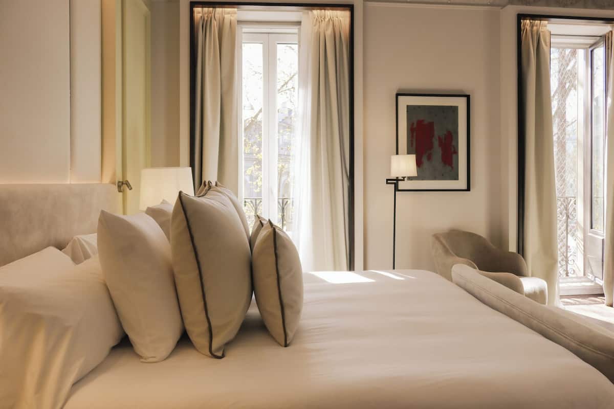 Een hotelkamer met een groot bed, een stoel, een lamp en een raam met gordijnen.