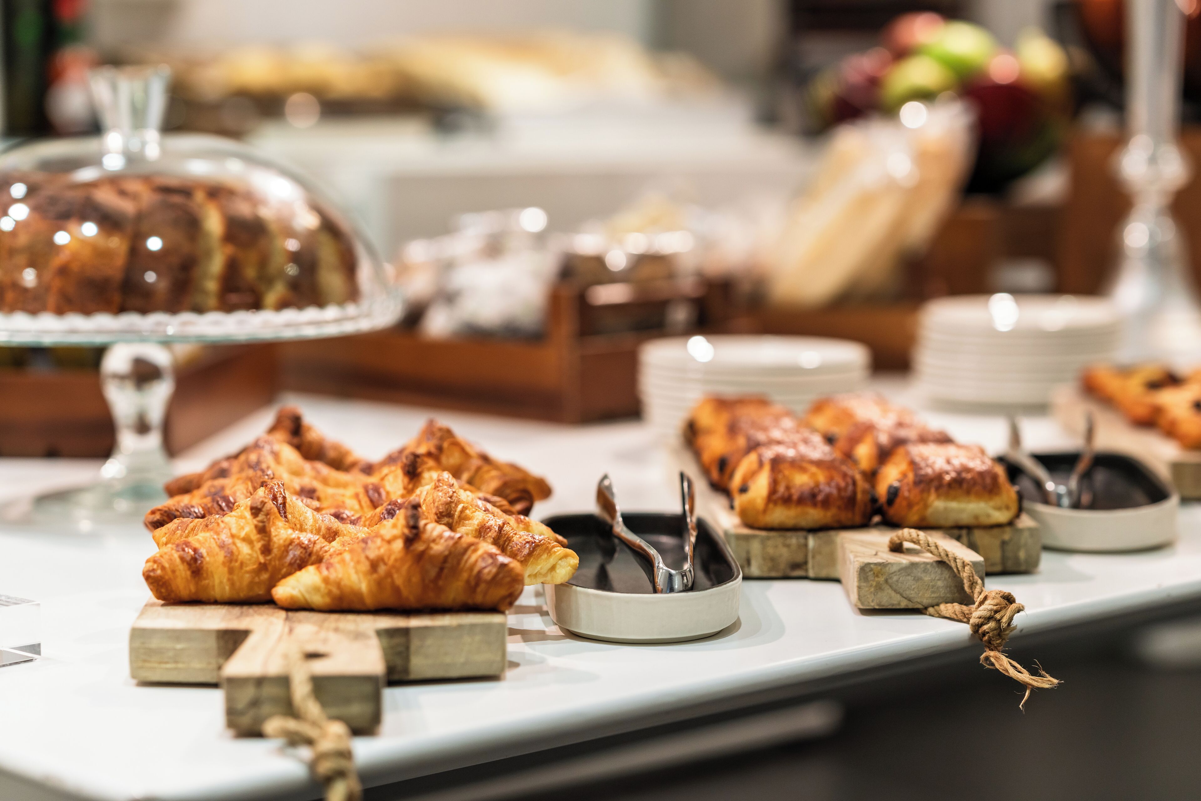 A buffet table with various baked goods, including pastries and a cake, arranged on wooden boards and a glass display.