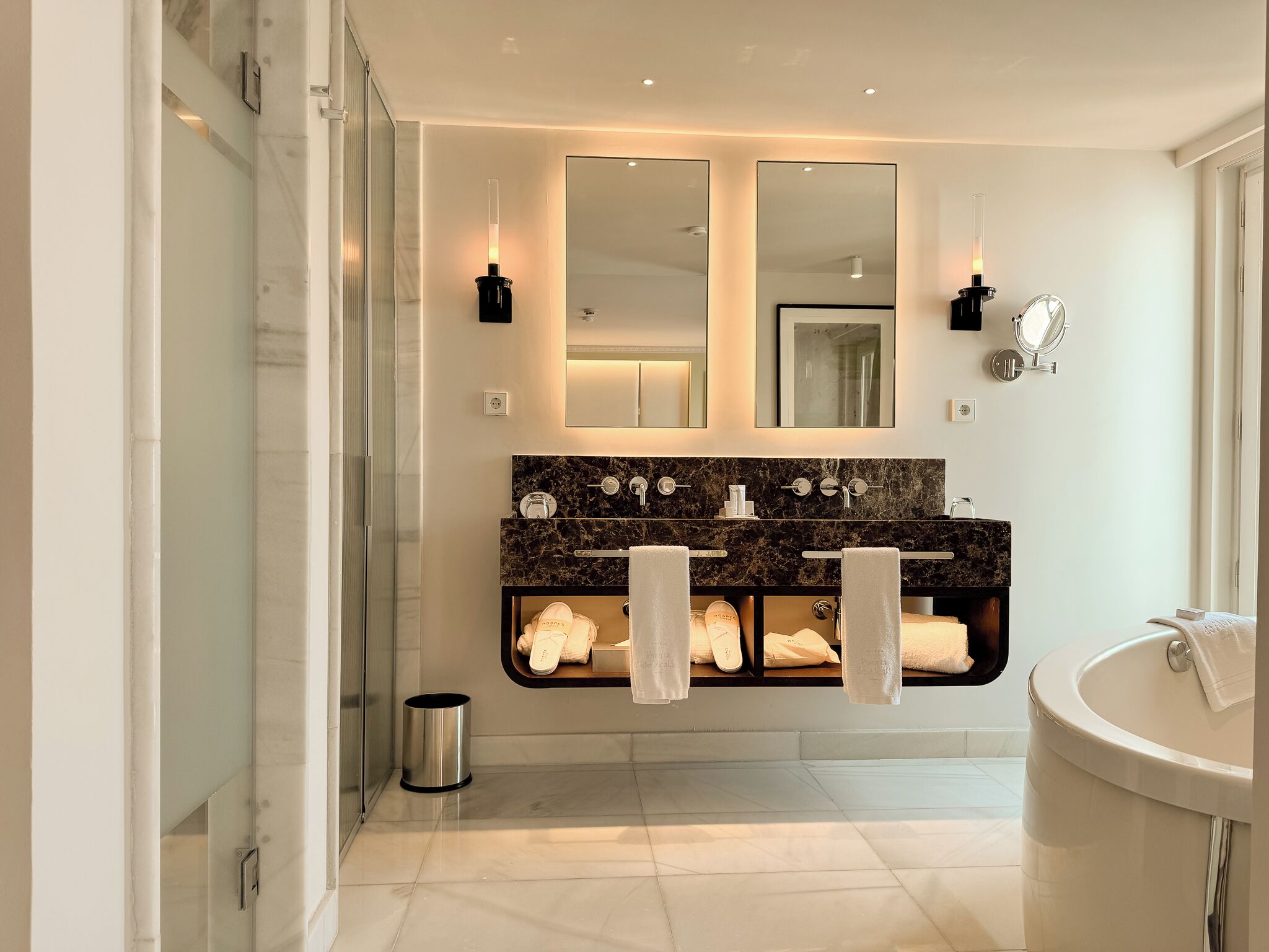 A modern bathroom with a marble countertop, two sinks, a large mirror, and a standalone bathtub.
