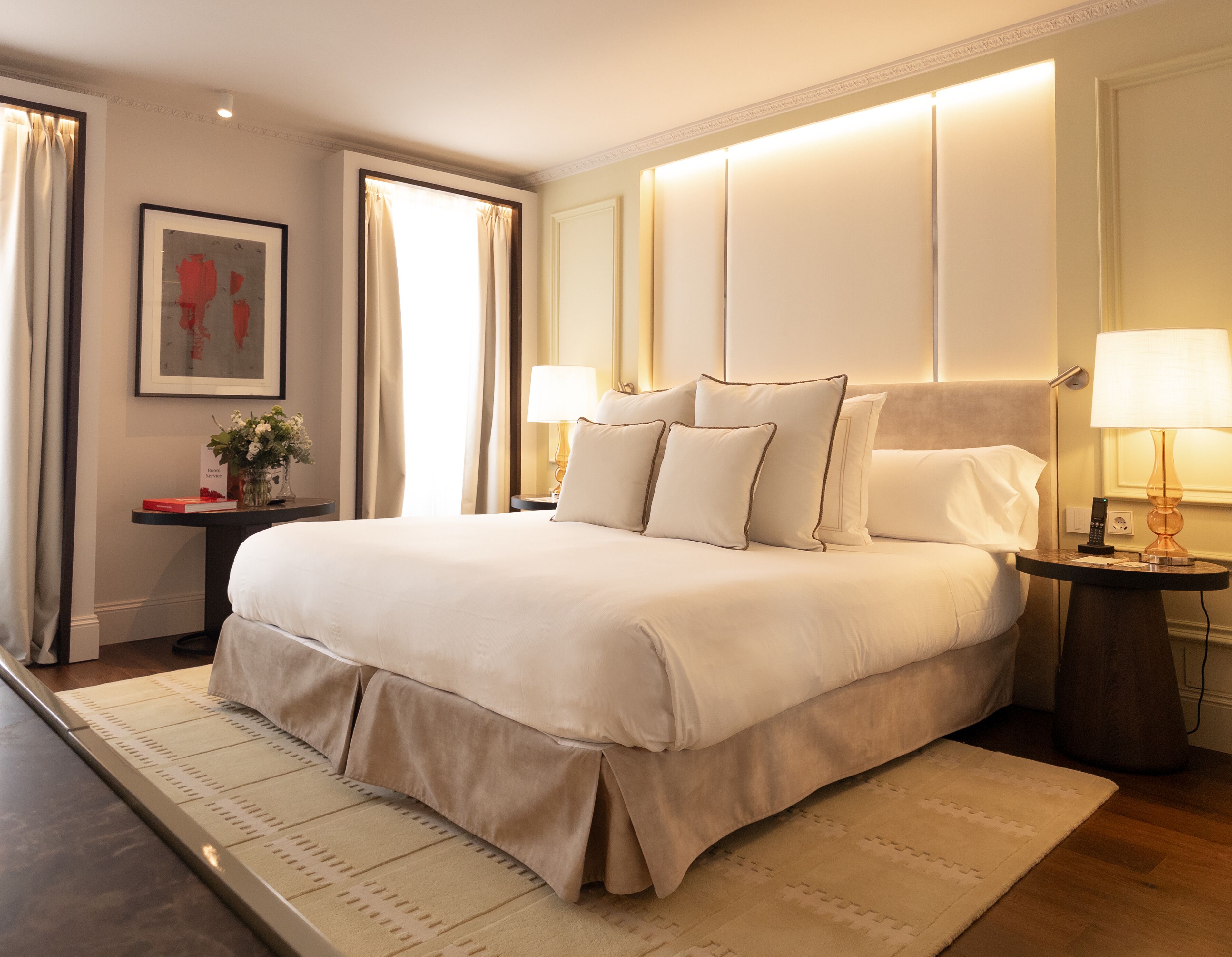 A neatly arranged hotel room with a large bed, bedside tables, a nightstand, and a wall-mounted lamp.