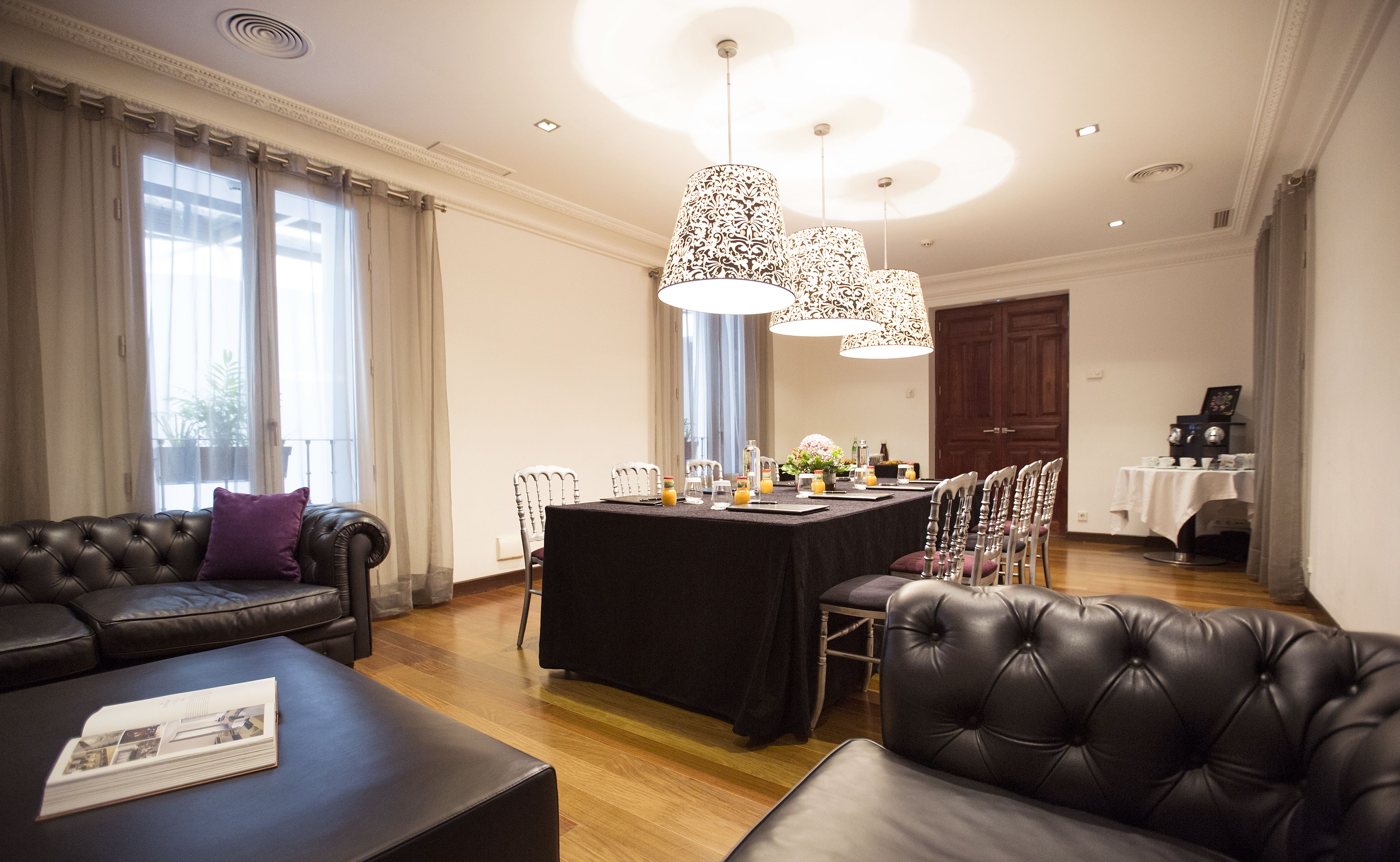 A modern hotel room with a dining area, a leather sofa, and a large window with curtains.