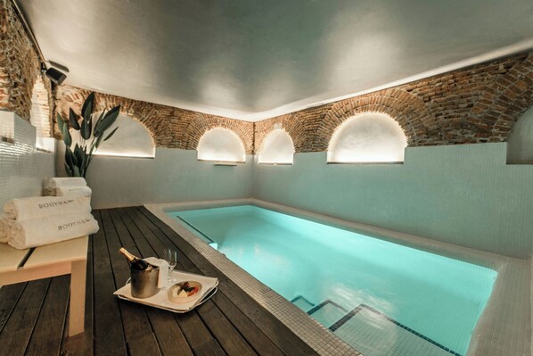 Zona de spa con piscina, terraza de madera y pared de ladrillo.