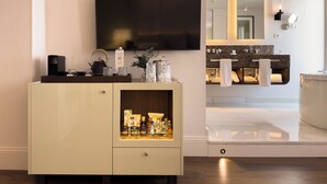 Un baño moderno con un espejo grande, un televisor de pantalla plana y un mueble de tocador con un perchero para toallas.