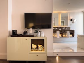 Un baño moderno con un espejo grande, un televisor de pantalla plana y un mueble de tocador con un perchero para toallas.