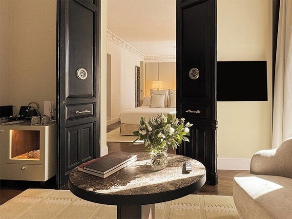Una habitación con una mesa redonda, un florero con flores, un sofá y una cama al fondo.