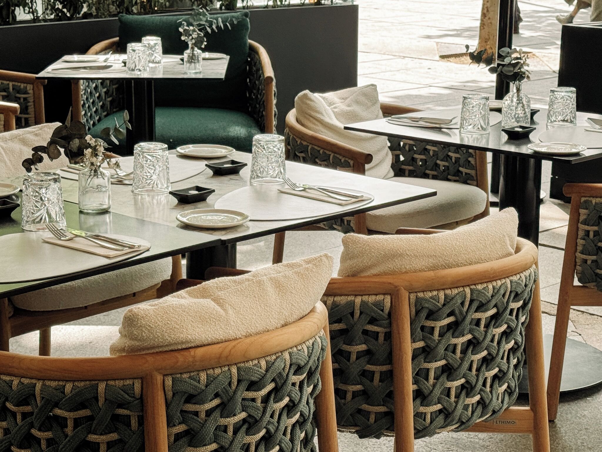 An outdoor dining area with round tables, cushioned chairs, and decorative glassware.