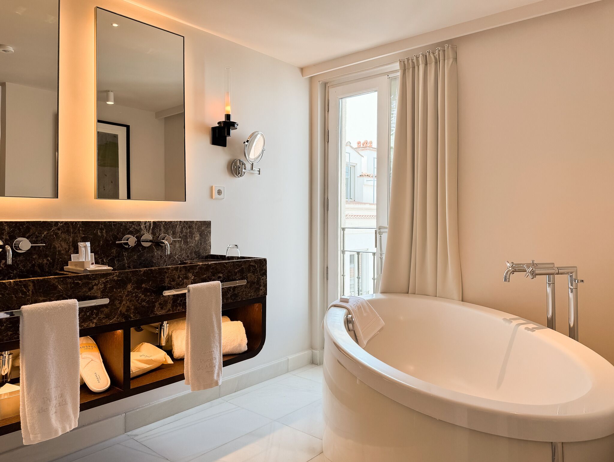 A modern bathroom with a large bathtub, dual sinks, a mirror, and a window with curtains.