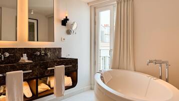 A modern bathroom with a large bathtub, dual sinks, a mirror, and a window with curtains.