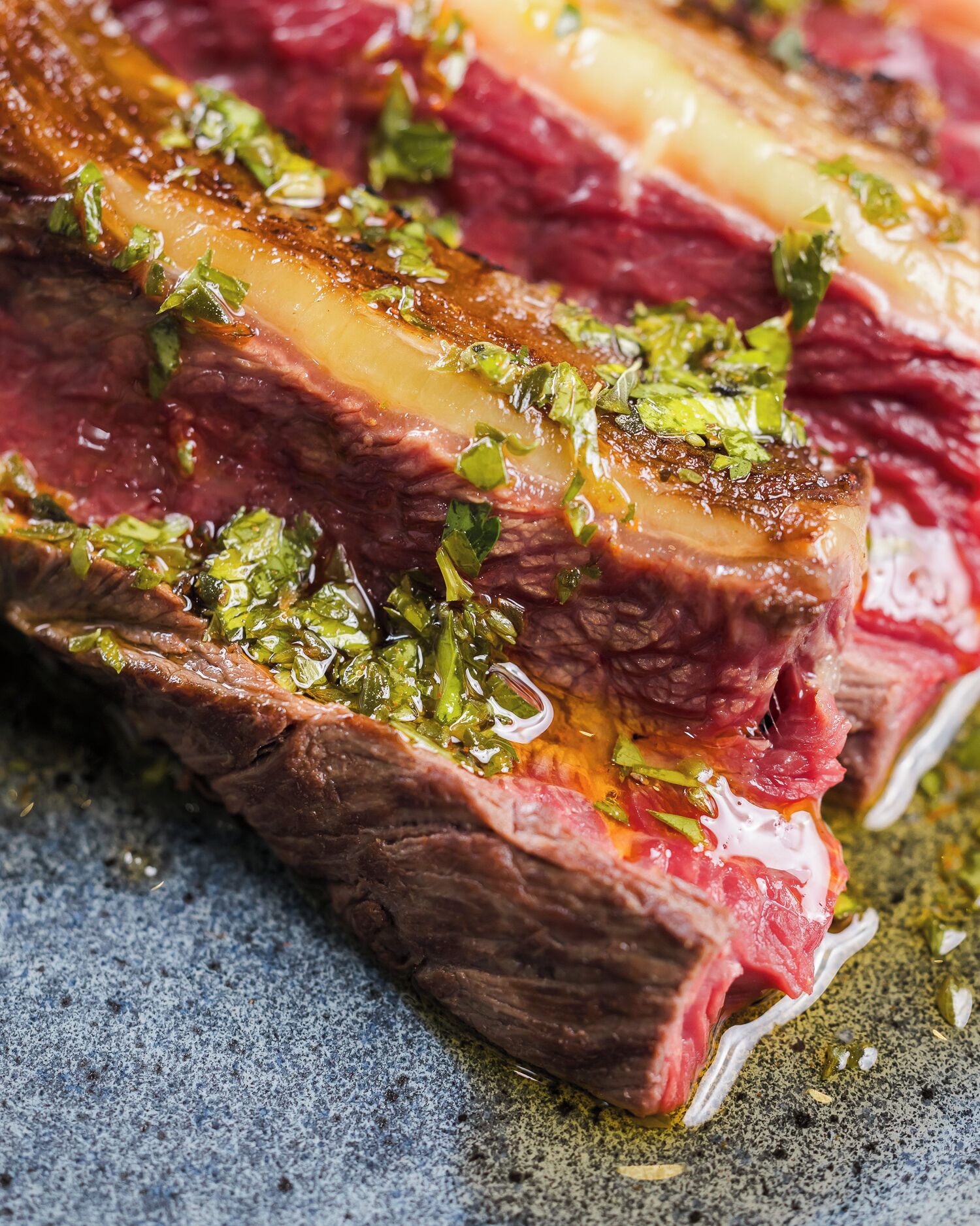 Une vue rapprochée d’un steak cuit, nappé d’une sauce brillante et parsemé d’herbes hachées.