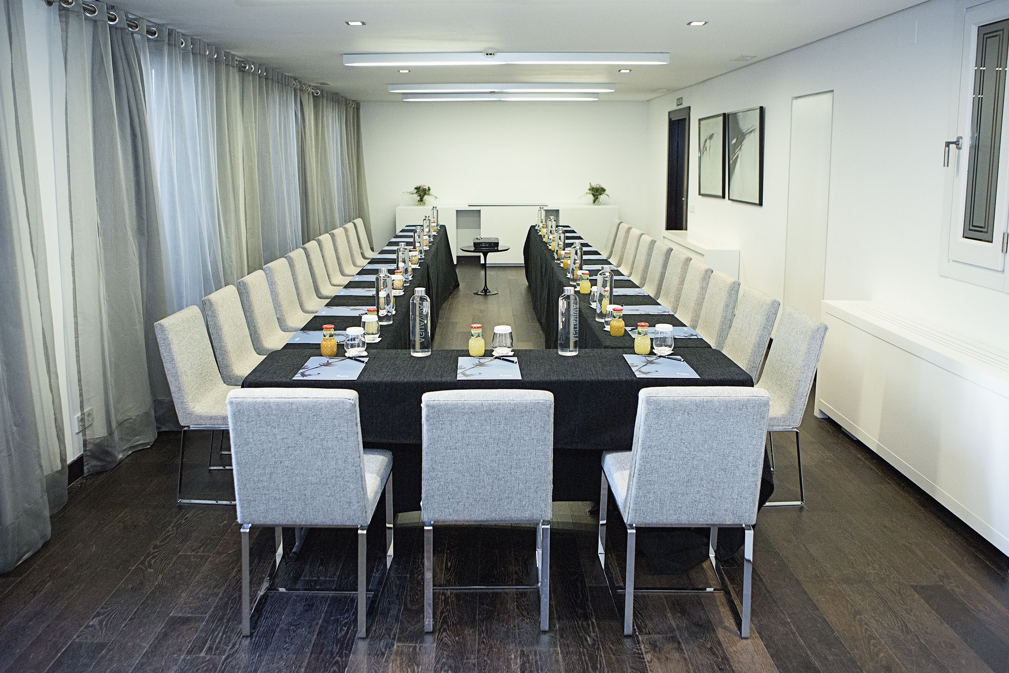 A conference room with a long table, grey chairs, and a small table in the center.