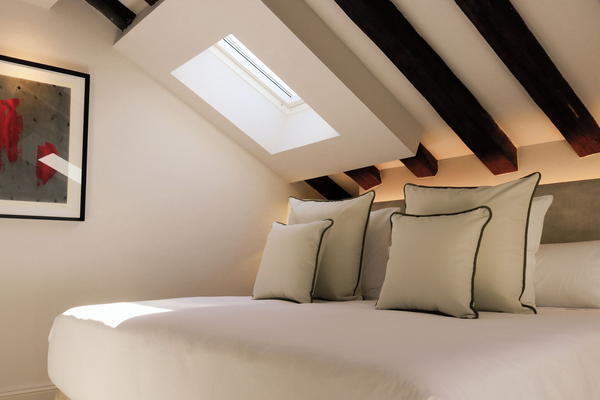 Ein Schlafzimmer mit Dachfenster, einem Bett mit Kissen und einem Bild an der Wand.