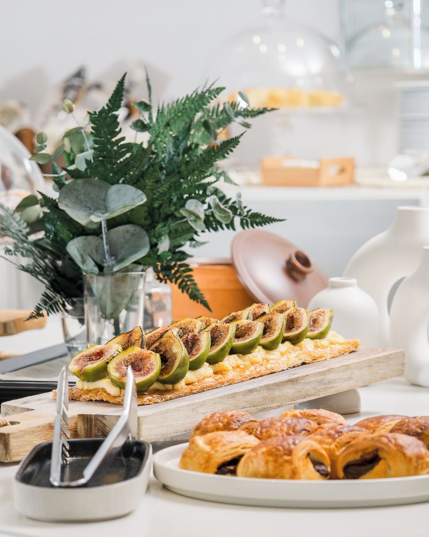 A breakfast setting with a plate of croissants, a fruit tart, and a decorative plant.