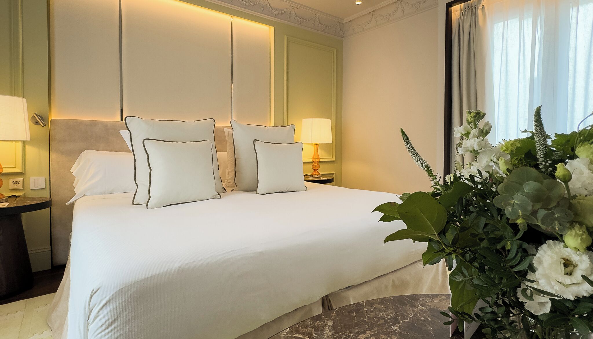 A hotel room with a large bed, two bedside lamps, a nightstand, and a potted plant.
