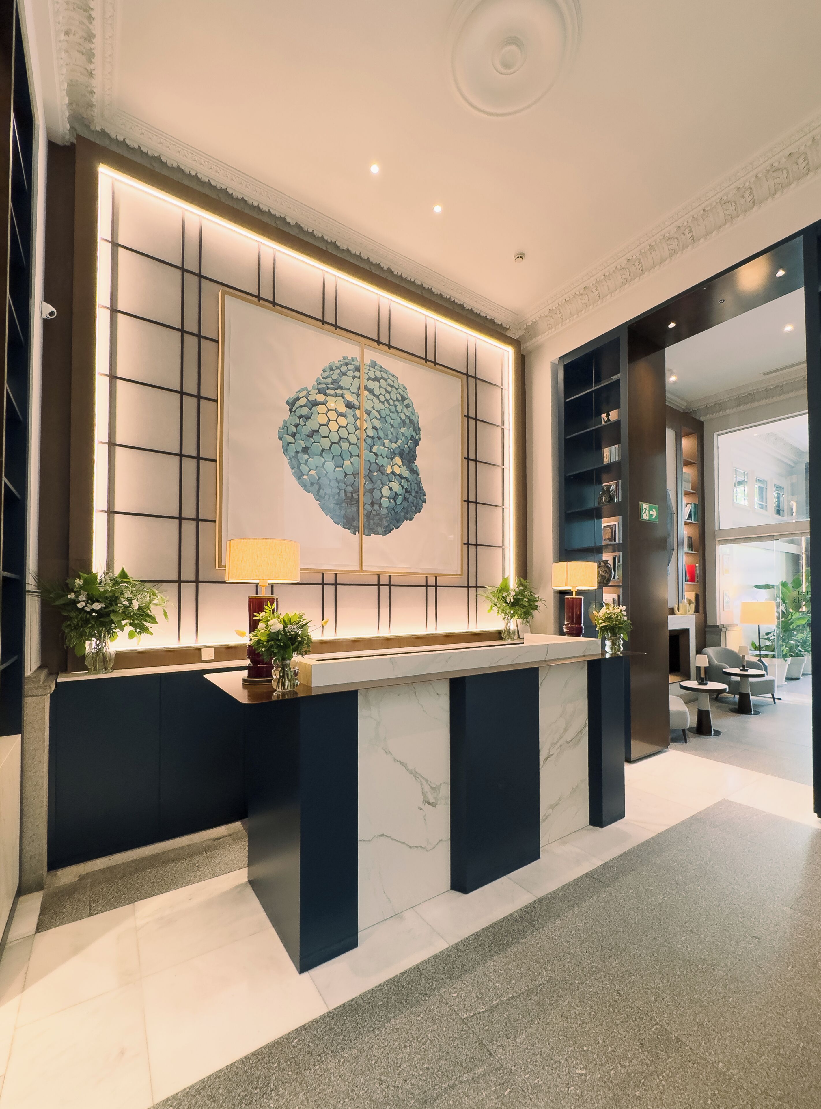 A reception desk with a marble top, flanked by two potted plants, and a large abstract artwork above.