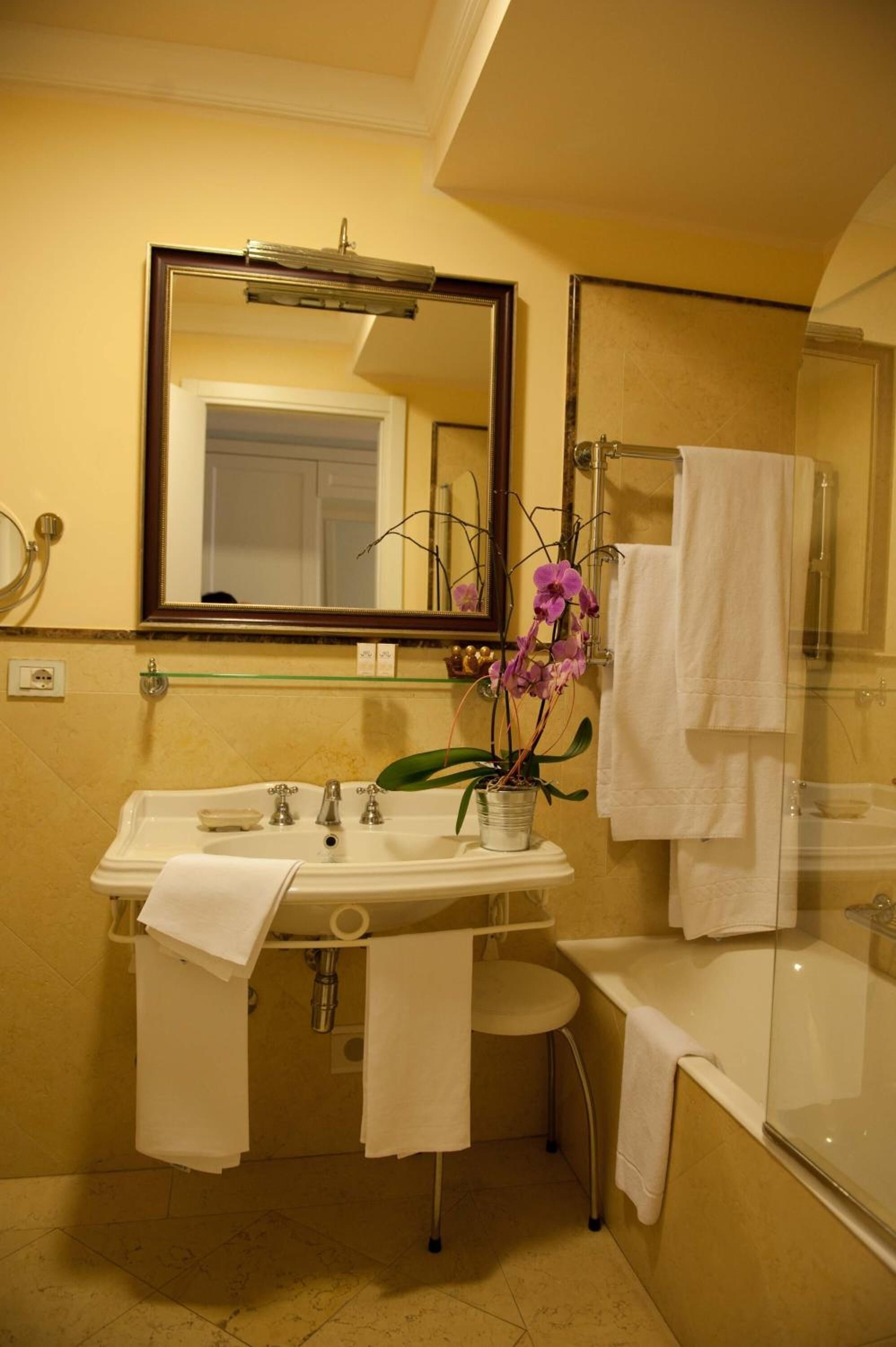 Ein Badezimmer mit Waschbecken, Spiegel und Badewanne. Handtücher hängen an der Wand und ein Blumentopf steht auf dem Waschbecken.
