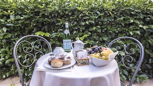 A table set outdoors with a bottle of Pellegrino water, a jug, a bowl of fruit, and pastries on a white tablecloth. - Hotel Villa Daphne (Giardini Naxos)