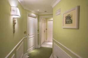 Un pasillo con paredes verdes, molduras blancas y una alfombra verde. Hay puertas blancas, un aplique en la pared y un cuadro enmarcado.